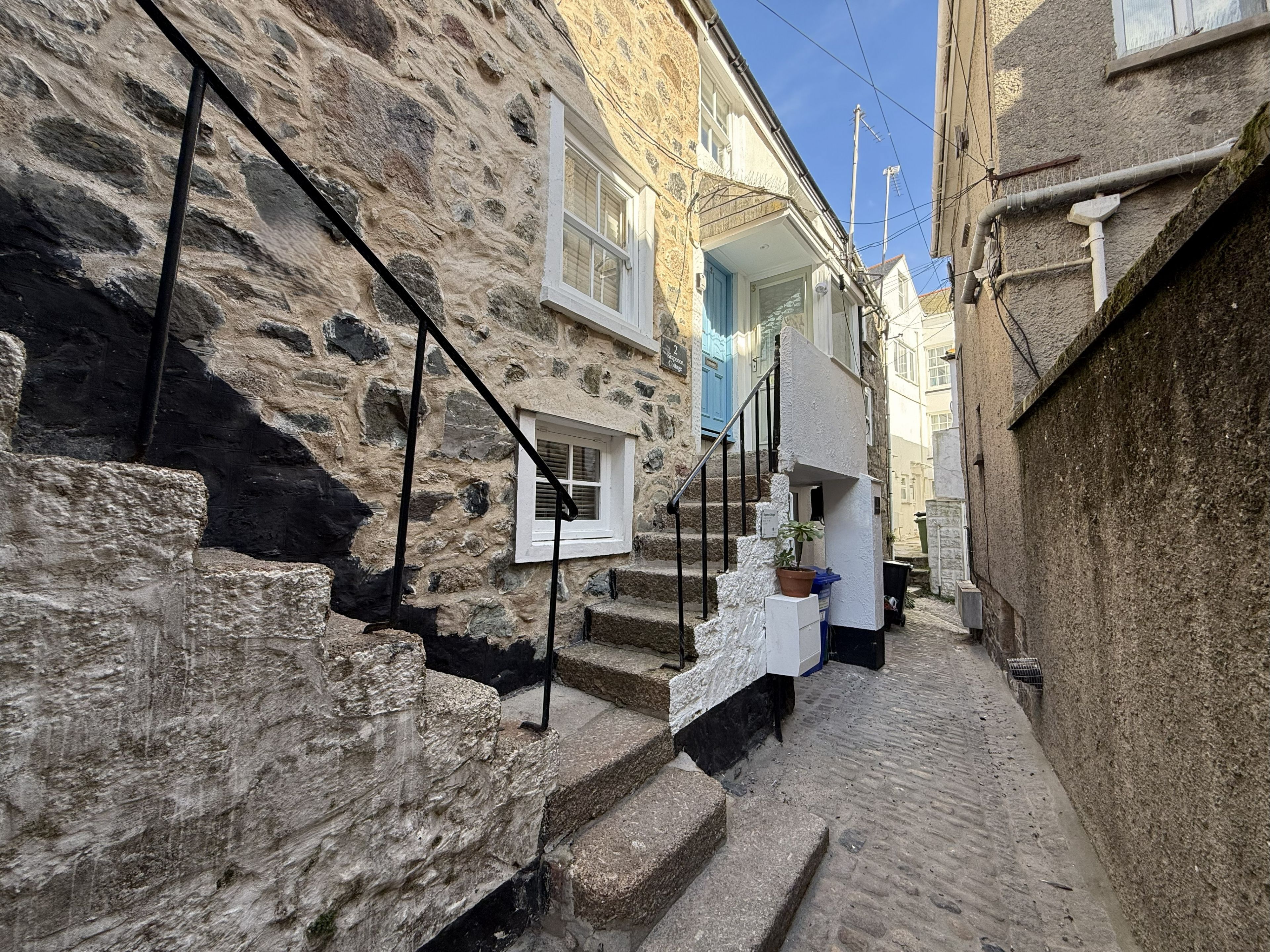 A narrow stone-walled alley with a staircase leading to a white door.