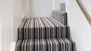 Un escalier recouvert d’une moquette à rayures, des murs blancs et un tableau encadré au-dessus.