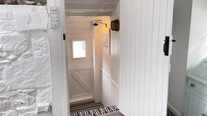 Un couloir intérieur aux murs blancs, avec une porte donnant sur une pièce dotée d’une fenêtre et d’un petit tableau accroché au mur.