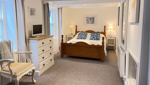 Une chambre à coucher avec un lit en bois, deux tables de chevet avec des lampes, une commode, une chaise et un téléviseur posé sur un meuble.