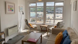Ein Wohnzimmer mit Blick auf einen Strand, inklusive Heizkörper, Lampe und einer Couch mit Kissen.