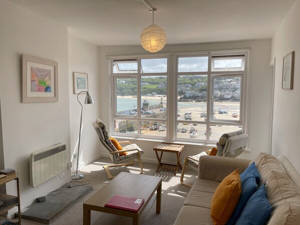 A living room with a view of a beach, a radiator, a lamp, and a sofa with cushions.