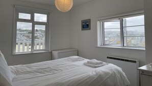 Ein Schlafzimmer mit einem Bett, zwei Fenstern, einer Heizung und einer Pendelleuchte.