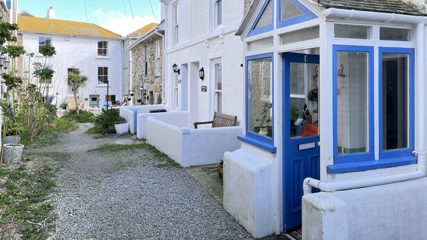 A narrow street with white buildings, a blue door, and a gravel path. - Sea Pebble - a cottage that sleeps 4 guests in 2 bedrooms (St Ives)
