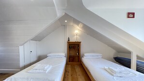 A small, clean room with two single beds, a wooden wardrobe, and a small table with a lamp. - Sea Pebble - a cottage that sleeps 4 guests in 2 bedrooms (St Ives)