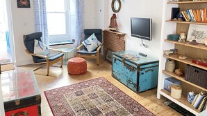 A cozy living room with a fireplace, a television, and a bookshelf filled with books and decorative items. - Sea Pebble - a cottage that sleeps 4 guests in 2 bedrooms (St Ives)