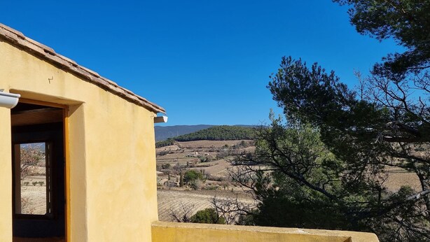 Ein gelbes Gebäude mit einem Ziegeldach, einer sichtbaren Tür und einem Fenster mit Blick auf eine hügelige Landschaft.