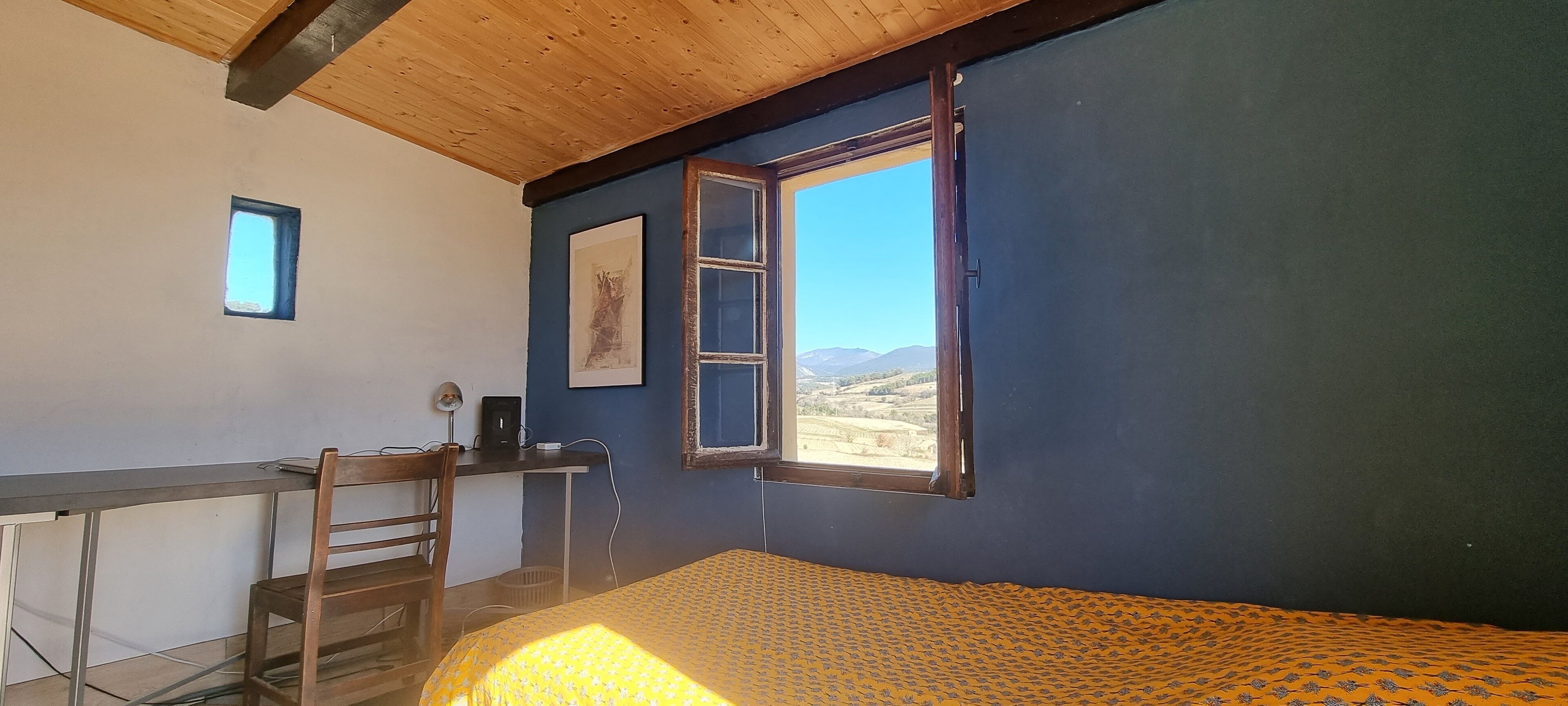 A room with a bed, a desk, a chair, a window, and a small picture on the wall.