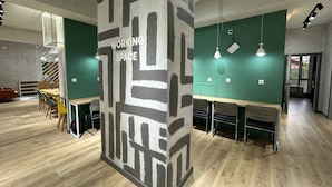 A modern workspace with a central pillar labeled "WORKING SPACE," wooden flooring, green walls, and multiple tables with chairs. - izzzi hostel Bishkek (Bishkek)