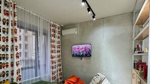 A modern living room with a green sofa, orange bean bag, and a flat-screen TV on the wall. - izzzi hostel Bishkek (Bishkek)