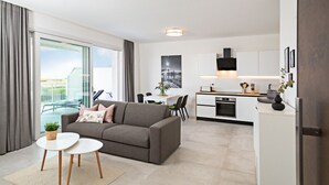 Un appartement moderne avec un canapé gris, un coin repas et une cuisine.