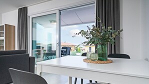 Un espace repas moderne avec une table blanche, des chaises grises et un vase vert contenant des plantes.