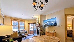 Una sala de estar acogedora con una mesa de comedor de madera, asientos cómodos, un televisor montado en la pared y una chimenea.