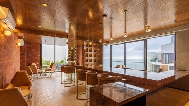 Un espace bar moderne avec un plafond en bois, des tabourets de bar et une grande fenêtre donnant sur la mer.