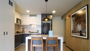 Une cuisine moderne avec des meubles blancs, un îlot central doté de tabourets de bar, un luminaire suspendu et un tableau encadré au mur.