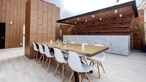 Un espace repas moderne avec une longue table en bois et des chaises blanches, un mur en briques agrémenté d’un motif de lattes en bois, et un comptoir en marbre.