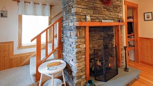 A cozy room with a stone fireplace, wooden beams, a small white table, and a staircase.