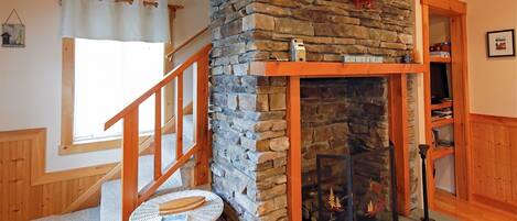 A cozy room with a stone fireplace, wooden beams, a small white table, and a staircase.