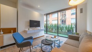 Ein modernes Wohnzimmer mit Flachbildfernseher, einer Couch, einem blauen Sessel und einem Glastisch.