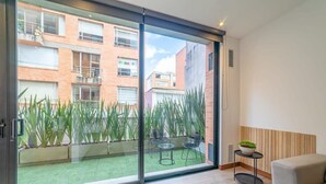 Eine moderne Wohnung mit einer Schiebetür, die auf einen Balkon mit Blick auf benachbarte Gebäude und einen kleinen Garten führt.