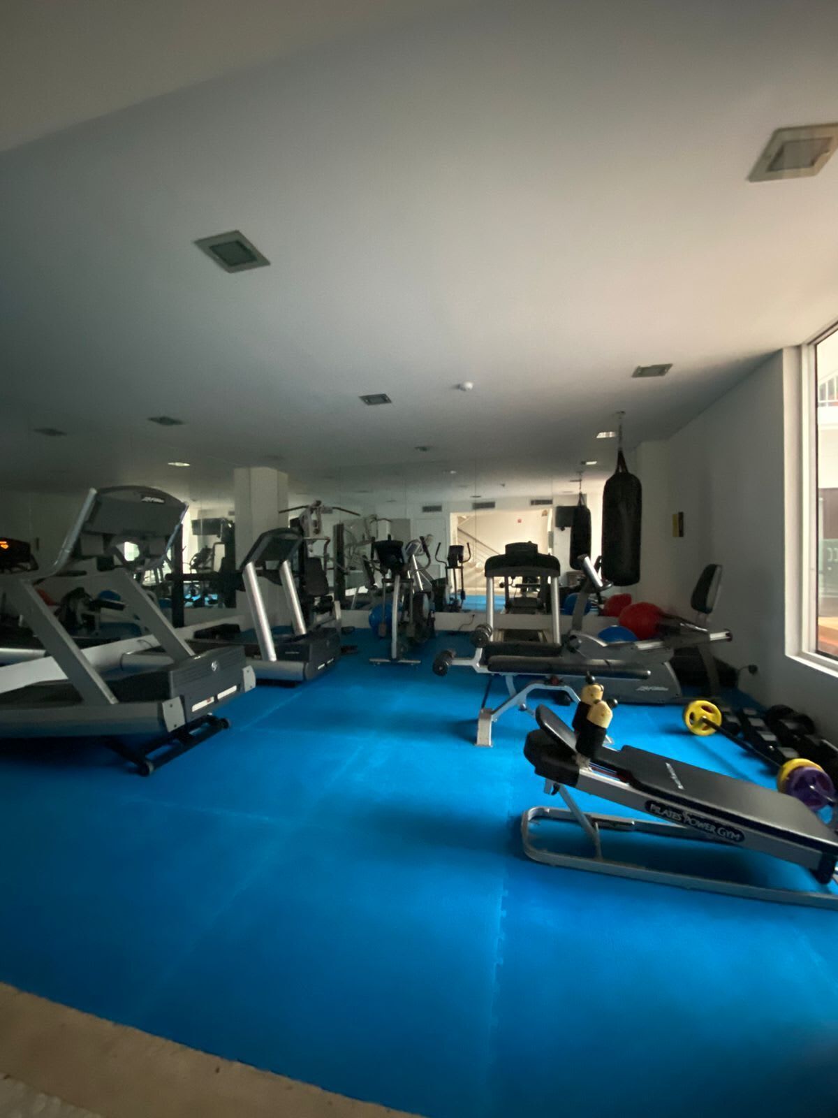 A gym with various exercise equipment, a blue floor, and a punching bag.
