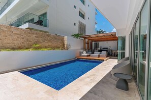 A modern outdoor pool area with a clear blue pool, a wooden deck, and a seating area with sofas and a table. - w* | Luxury 4BR w/ Private Pool in Morros Epic (Cartagena de Indias)