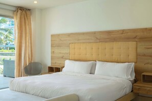 Habitación de hotel con una cama grande, cabecera de madera, dos mesitas de noche y vistas a un balcón con plantas.