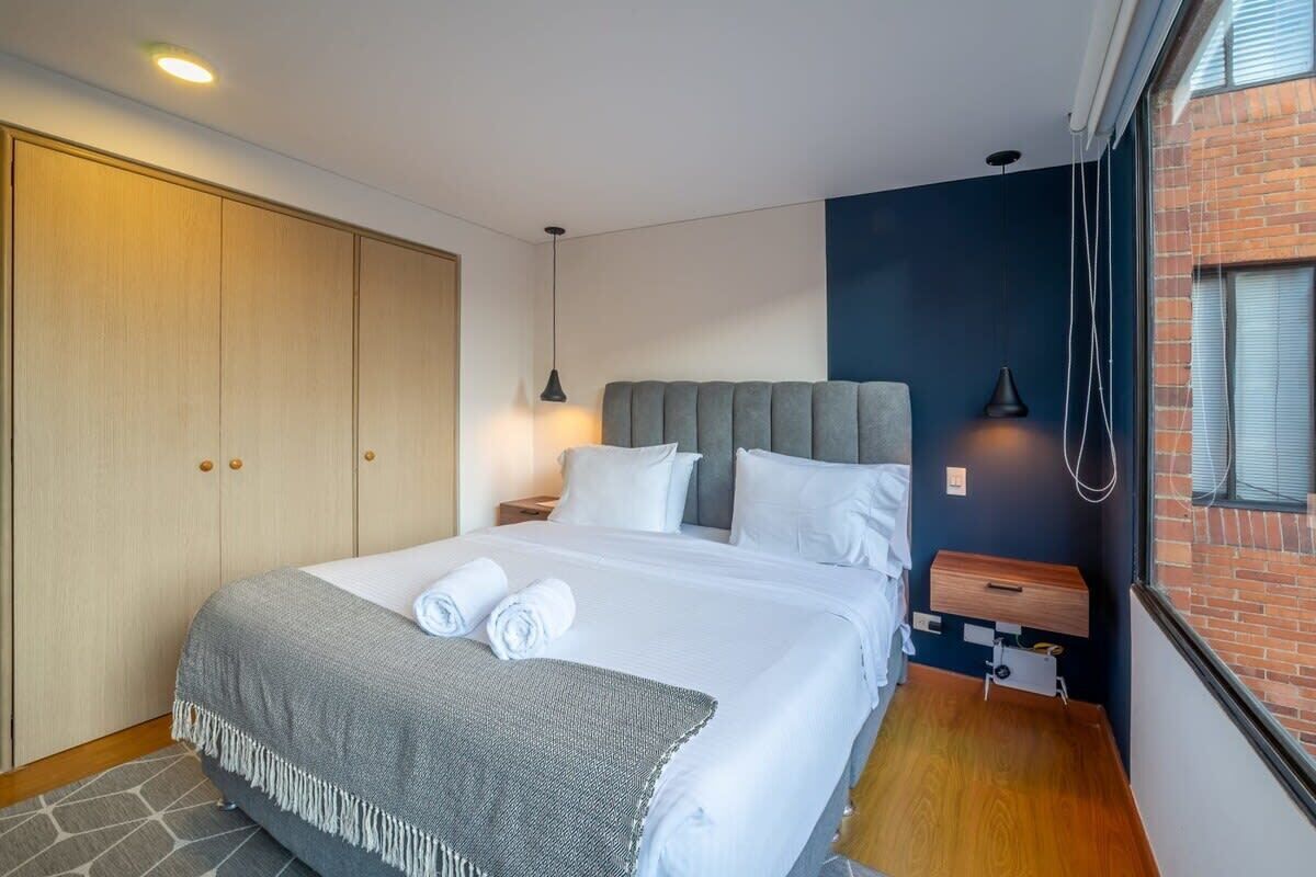 A modern hotel room with a large bed, a wardrobe, a bedside table, and a view of a brick wall.