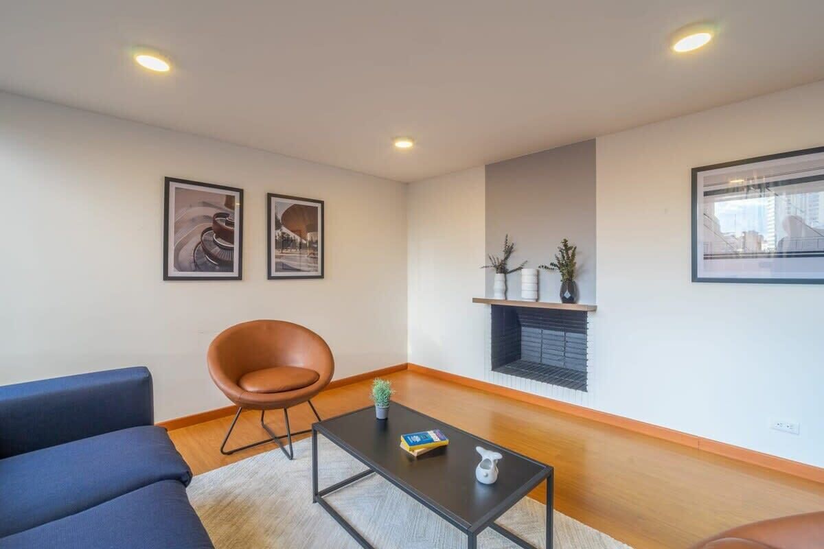 A modern living room with a blue sofa, a brown chair, a black coffee table, and framed artwork on the walls.