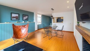 Una cocina moderna con encimera de madera, una zona de comedor con sillas de metal y un televisor grande montado en la pared.