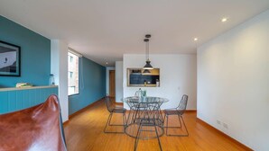 Un interior moderno con zona de comedor que incluye una mesa de vidrio y sillas de metal, un sillón de cuero marrón y una lámpara colgante.