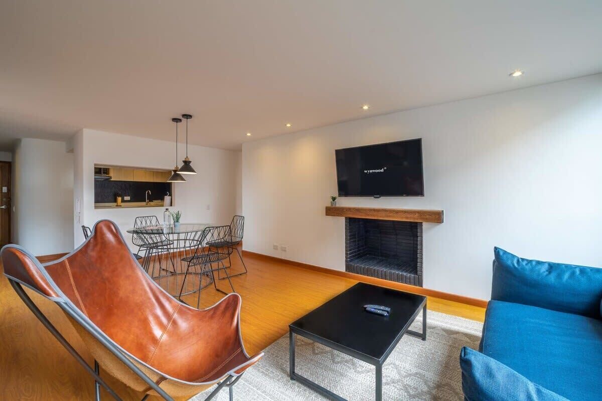 A modern living room with a fireplace, a dining area with a table and chairs, and a television mounted on the wall.