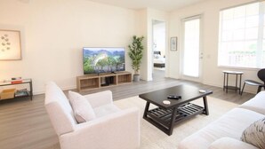 Una sala de estar moderna con una televisión de pantalla plana, dos sofás, una mesa de centro y una planta en maceta.