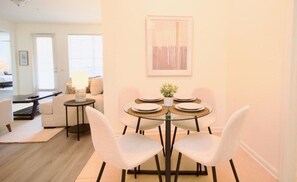 A dining area with a round glass table, white chairs, and a small side table with a lamp. - New! Vista Cay Luxury Mirage 2 Bedroom Condo by RedAwning (Orlando)