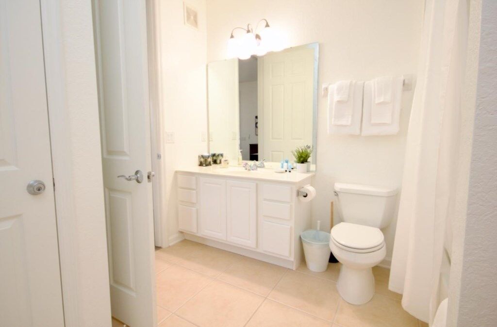 Un bagno con un WC bianco, un lavandino con uno specchio sopra e un cestino.