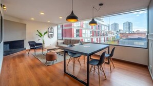 A modern living room with a fireplace, a dining area, and large windows offering a city view. - w* | Industrial 1BR In Cabrera (Bogotá)