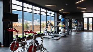 Une salle de sport équipée de machines de cardio, d’appareils de musculation et dotée d’une grande fenêtre offrant une vue sur la ville.