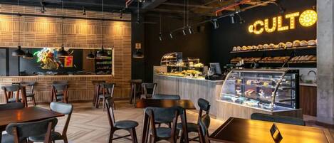 Een modern caféinterieur met houten vloeren, zwart-grijze stoelen, een balie met een vitrine en een neonbord met de tekst 'CULTO'.