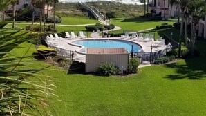 A pool area with lounge chairs, a wooden deck, and a view of the ocean.