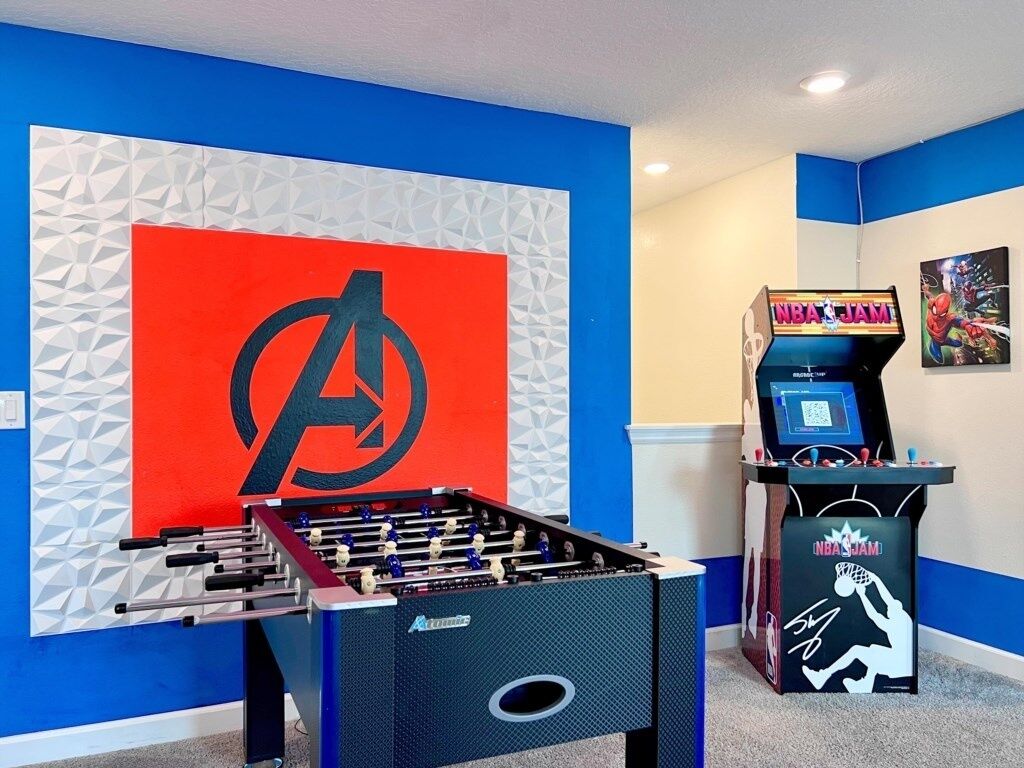 A room with a foosball table, a wall with a large logo, and an arcade machine.