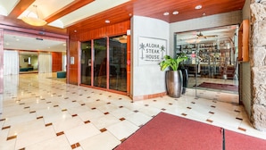 Un'accogliente hall d'hotel dal design moderno, caratterizzata da un pavimento a scacchi, una reception e un'insegna per Aloha Steak House.