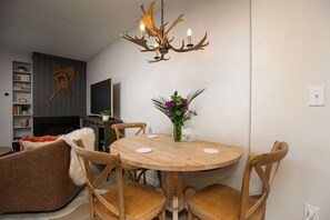 Un comedor con una mesa redonda de madera, cuatro sillas de madera, una araña, una chimenea y una estantería.