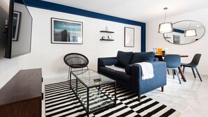 Ein modernes Wohnzimmer mit einer Couch, einem Glastisch, einem Streifen Teppich, einem Fernseher und einem Essbereich mit Stühlen und Tisch.