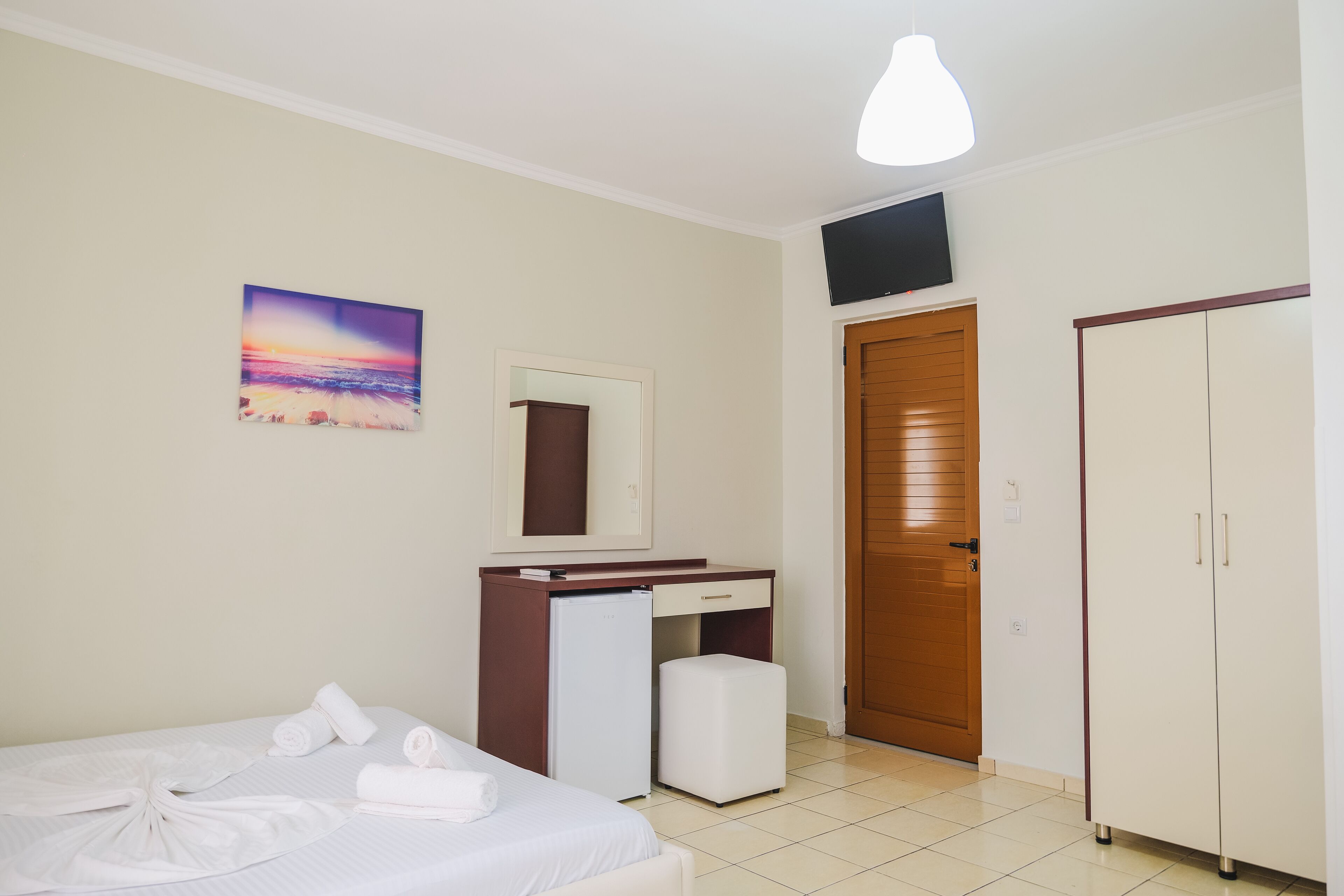 Una habitación de hotel con cama, escritorio, refrigerador pequeño, televisor y armario.