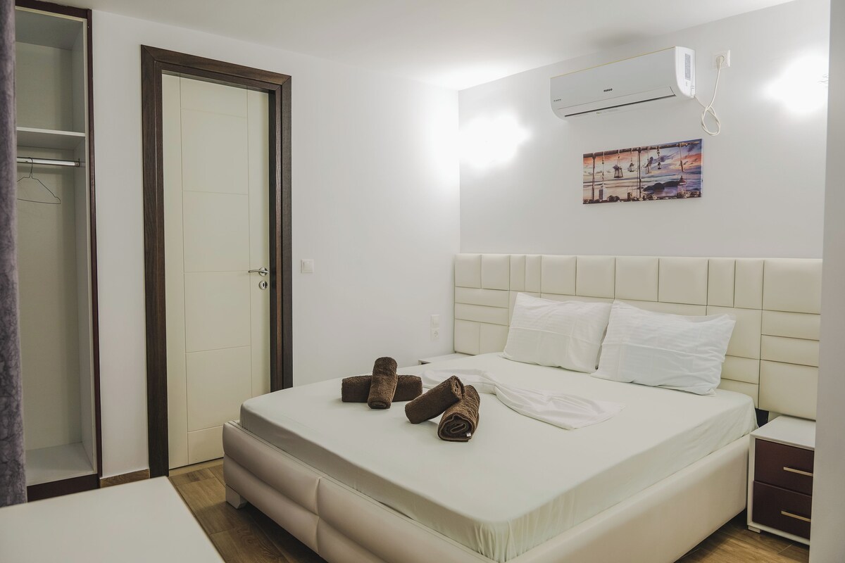 A hotel room with a bed, a bedside table, a nightstand, a wardrobe, and an air conditioning unit.