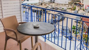 A balcony with wicker chairs and a table, overlooking a street with parked cars and buildings. - Foris Rooms (Himarë)