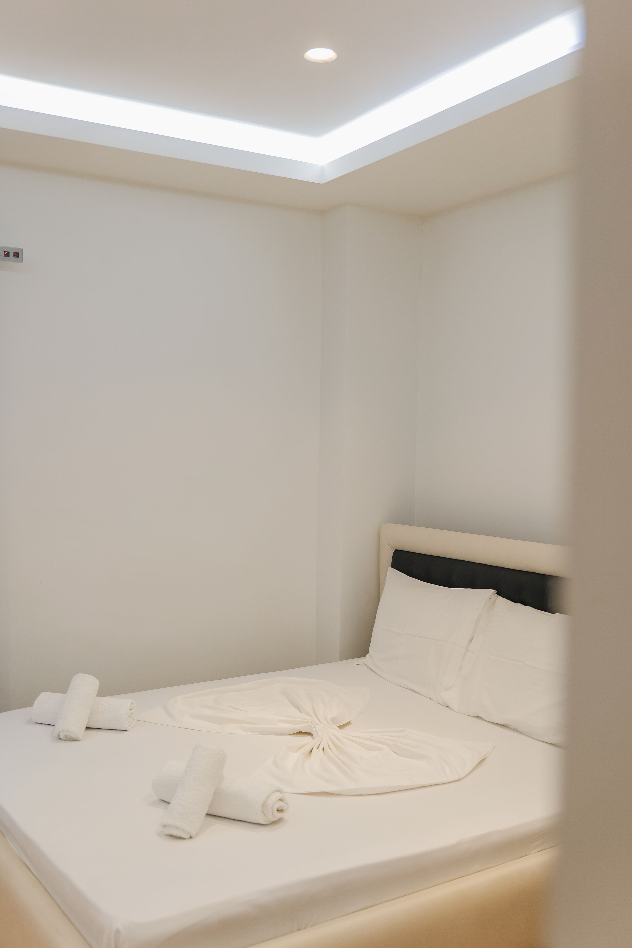 A neatly made bed with white linens and towels, a headboard, and a ceiling light fixture.