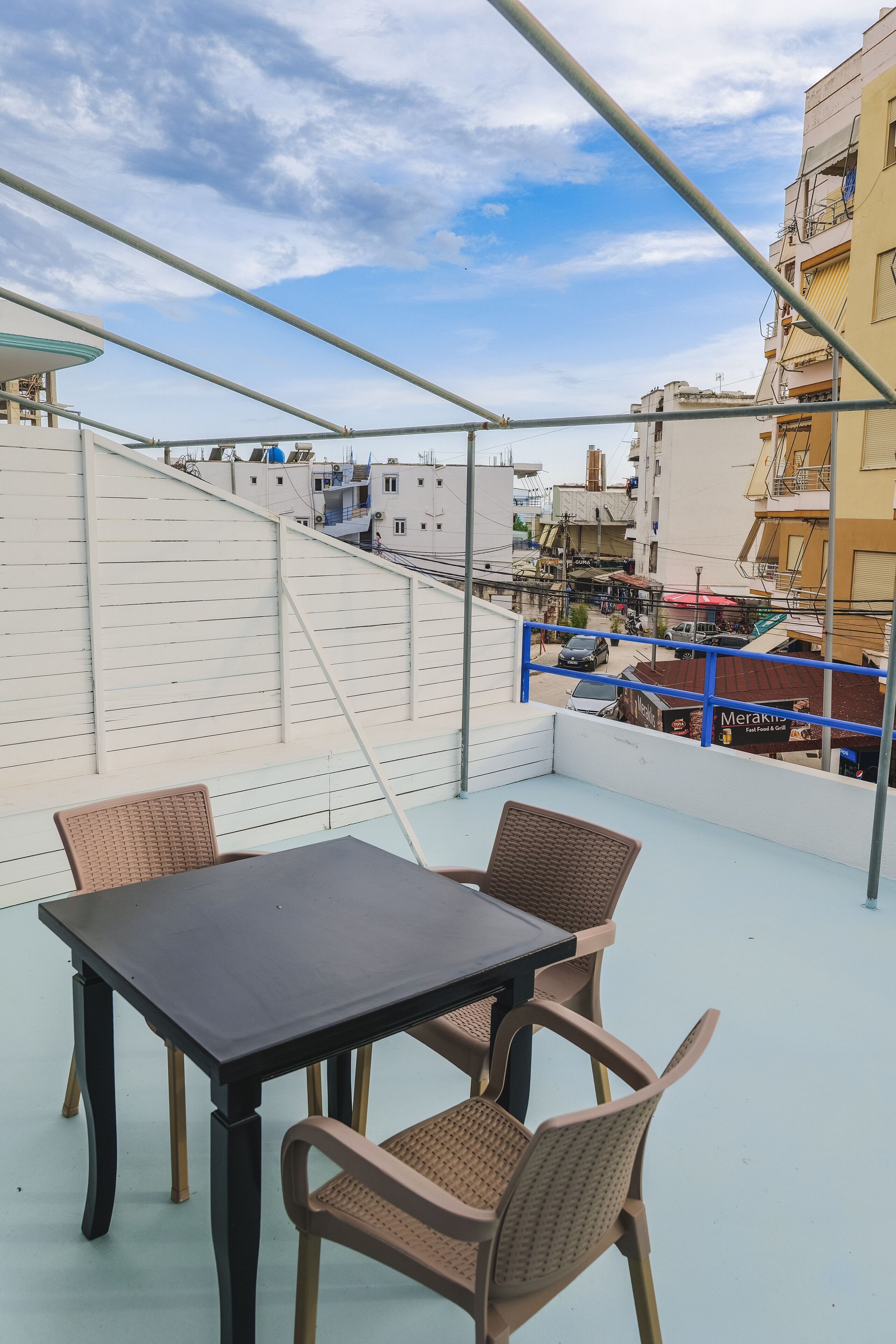 A rooftop terrace with a table and chairs, overlooking a cityscape with buildings and a street.