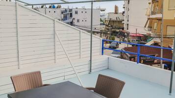 A rooftop terrace with a table and chairs, overlooking a cityscape with buildings and a street.