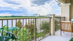 A balcony with a view of a river and distant buildings, a chair, and a table. - Lakeview Penthouse Elegance 3 Bedroom Condo by RedAwning (Orlando)